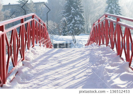 Red metal pedestrian bridge covered with snow in a sunny winter park 136512453