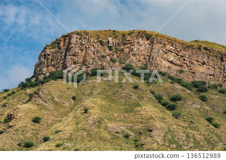 Rocky cliff on grassy hillside under blue sky in rural Rajasthan, India Rocky cliff on grassy hillside under blue sky in rural Rajasthan, India 136512989