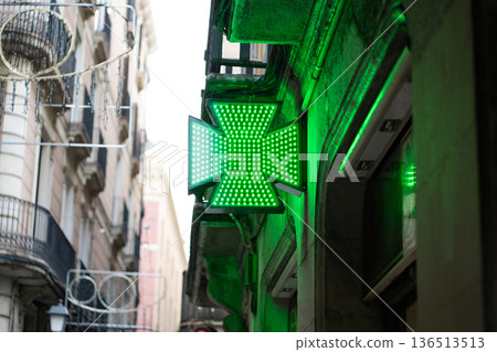 Green LED pharmacy cross illuminating a historic European street building, representing healthcare, medicine, and wellness services at a traditional drugstore Green LED pharmacy cross illuminating a historic European street building, representing healthcare, medicine, and wellness services at a traditional drugstore 136513513