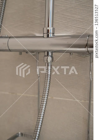 Chrome shower faucet and flexible hose connecting to a modern mixer tap in a tiled bathroom, reflecting light and offering a close-up view of plumbing fixtures 136513527