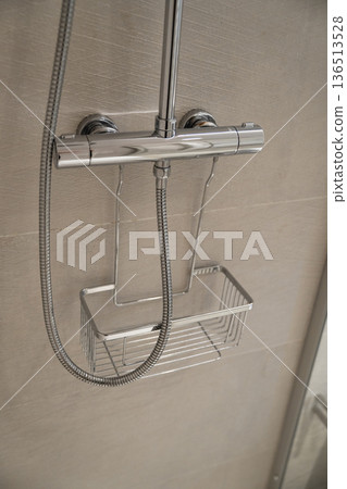 Chrome shower faucet with a thermometer and a shower hose hanging on a stainless steel wire basket, providing a modern and functional bathroom design Chrome shower faucet with a thermometer and a shower hose hanging on a stainless steel wire basket, providing a modern and functional bathroom design 136513528