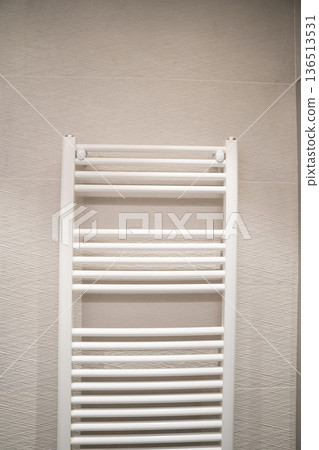 White bathroom towel rail heater providing warm comfort in a modern home interior, ensuring ready-to-use dry towels in a contemporary hotel or residential space White bathroom towel rail heater providing warm comfort in a modern home interior, ensuring ready-to-use dry towels in a contemporary hotel or residential space 136513531