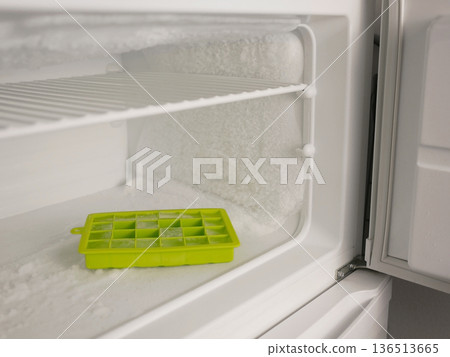 Close up of ice tray inside heavily frosted freezer. Home appliance with ice buildup, cold storage problem, defrosting and energy efficiency concept for kitchen maintenance themes Close up of ice tray inside heavily frosted freezer. Home appliance with ice buildup, cold storage problem, defrosting and energy efficiency concept for kitchen maintenance themes 136513665