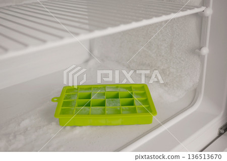 Close up of ice tray inside heavily frosted freezer. Home appliance with ice buildup, cold storage problem, defrosting and energy efficiency concept for kitchen maintenance themes 136513670
