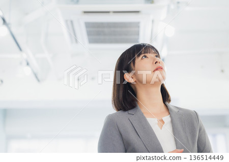 一位面露不滿的女商人看著冷氣。 一位面露不滿的女商人看著冷氣。 136514449