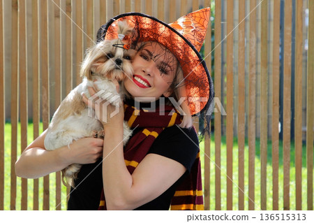 A beautiful girl is sitting on the terrace with a dog, holding a pumpkin in her hand. A beautiful girl is sitting on the terrace with a dog, holding a pumpkin in her hand. 136515313