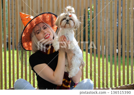 A beautiful girl is sitting on the terrace with a dog, holding a pumpkin in her hand. 136515390