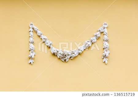 Elegant white plaster garland mounted on yellow wall 136515719