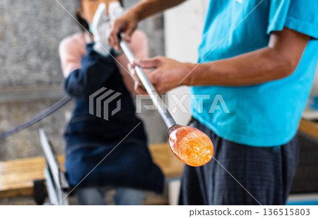 The production process of shaping molten glass onto the tip of a rod in a glassblowing workshop The production process of shaping molten glass onto the tip of a rod in a glassblowing workshop 136515803