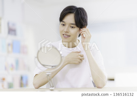 Men's Beauty: A smiling young Japanese man touching his hair while looking in the mirror Men's Beauty: A smiling young Japanese man touching his hair while looking in the mirror 136516132