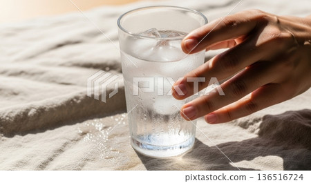 Refreshing Glass of Ice Water Held by Hand on Linen Background 136516724