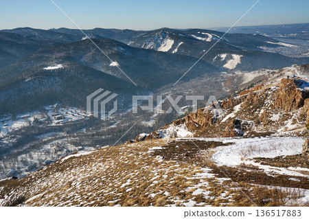 Scenic winter mountain landscape with snowy peaks and a valley with a small village. Nature beauty and tranquil outdoor exploring concept. Torgashinsky ridge, Krasnoyarsk, Siberia Scenic winter mountain landscape with snowy peaks and a valley with a small village. Nature beauty and tranquil outdoor exploring concept. Torgashinsky ridge, Krasnoyarsk, Siberia 136517883