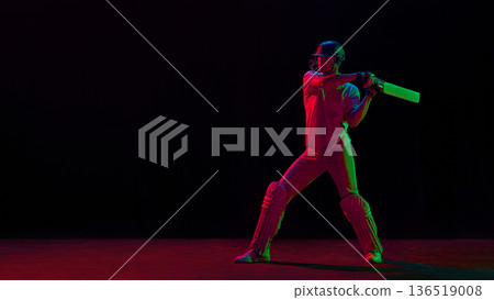 Cricket batsman in ready stance under red and green neon lighting. Cricket batsman in ready stance under red and green neon lighting. 136519008
