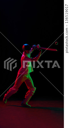 Cricket player hitting ball under red and green neon lighting 136519017