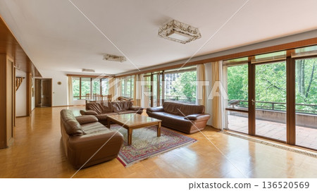 A spacious living room with wooden floors and large windows overlooking a beautiful forest in a private house. A spacious living room with wooden floors and large windows overlooking a beautiful forest in a private house. 136520569
