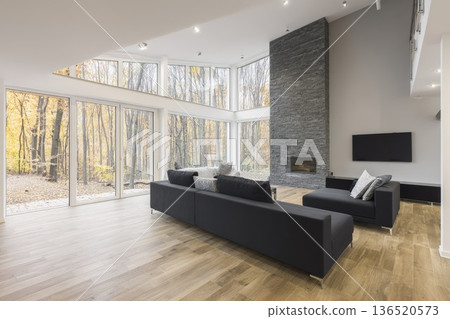 A spacious ground-floor living room with mixed wood and laminate flooring and large windows facing a forest. 136520573