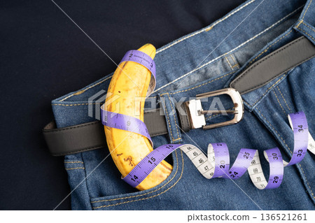 Banana with measuring tape on jean trousers, penis health. Banana with measuring tape on jean trousers, penis health. 136521261