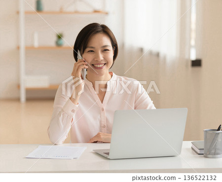 A woman talking on her smartphone while working from home 136522132
