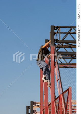 Freerunner climbing red metal structure during parkour training session 136522489