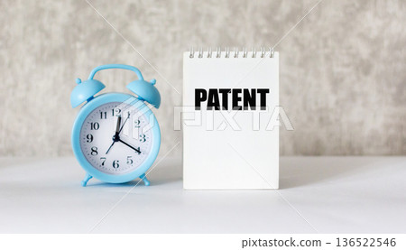 The PATENT text on a notebook on a beige background next to the clock The PATENT text on a notebook on a beige background next to the clock 136522546
