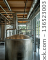 Modern brewery interior with large stainless steel tanks and industrial pipes 136523003