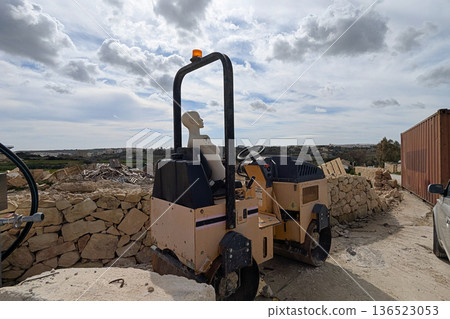 Classical white statue seated on yellow road roller near rocky coast, surreal contemporary art mood with cloudy sky Classical white statue seated on yellow road roller near rocky coast, surreal contemporary art mood with cloudy sky 136523053