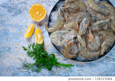 Fresh raw shrimp spread on ice with lemon and cilantro slices on a marble surface, ready to cook, no people Fresh raw shrimp spread on ice with lemon and cilantro slices on a marble surface, ready to cook, no people 136523068
