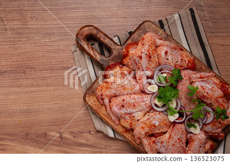 Chicken wings, marinated and laid out on a wooden platter, ready for cooking, grilling or baking, in a home kitchen, there are no people 136523075