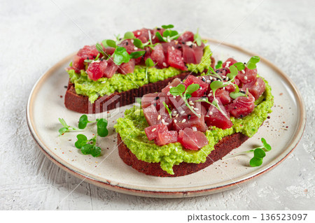 toasts with fresh tuna and avocado, spread on black bread and sprinkled with microgreens, breakfast, healthy food 136523097