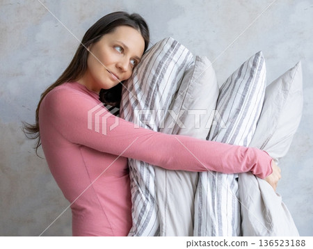 woman holds pile of pillows in her hands. pillows are in different colors, look like stack. woman holds pile of pillows in her hands. pillows are in different colors, look like stack. 136523188