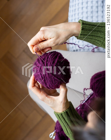 women's hands wind wool yarn into a ball. woman knits wool clothes on knitting needles. women's hands wind wool yarn into a ball. woman knits wool clothes on knitting needles. 136523192