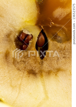 a cut yellow apple with a large orange spot during rotting, one apple on a black wooden table made of pine wood cut into two halves, the apple is rotten inside 136523575