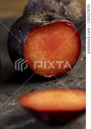 sliced black fresh juicy plums on the kitchen table, some beautiful black plums on the table, plum with red juicy sweet flesh cut into pieces 136523636