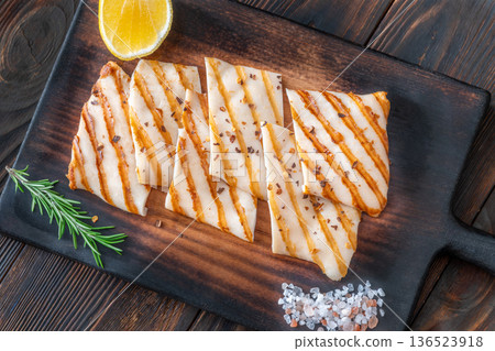 Grilled squid steaks with rosemary and lemon on dark wooden cutting board Grilled squid steaks with rosemary and lemon on dark wooden cutting board 136523918