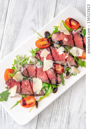 Italian beef tagliata salad with arugula and balsamic glaze on white plate Italian beef tagliata salad with arugula and balsamic glaze on white plate 136523923