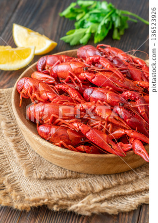 Wooden bowl of bright red boiled crawfish with lemon and parsley, rustic table 136523926