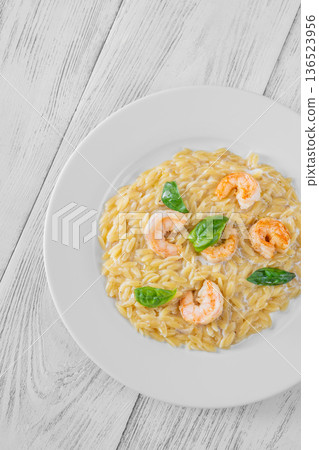 Creamy orzotto pasta topped with grilled prawns and fresh basil on rustic wooden table 136523956