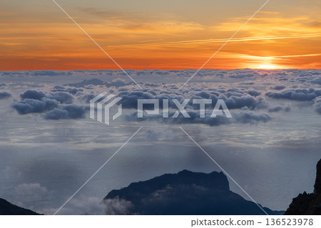 At Pico do Arieiro viewpoint, Madeira, dawn light spreads over layered clouds and a calm sea below 136523978