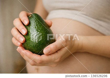 Maternity healthy lifestyle concept. Pregnant woman with avocado as symbol of baby size and nutrition. 136526206