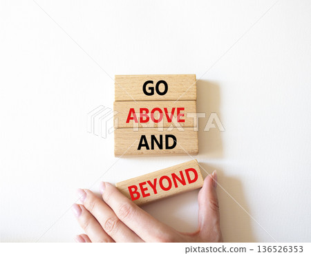 Go above and beyond symbol. Concept words Go above and beyond on wooden blocks. Beautiful bright white background. Businessman hand. Business and Go above and beyond concept. Copy space. Go above and beyond symbol. Concept words Go above and beyond on wooden blocks. Beautiful bright white background. Businessman hand. Business and Go above and beyond concept. Copy space. 136526353