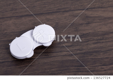 A white contact lens case placed on a wood grain background 136527724