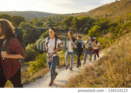 Group of people with backpacks hiking or trekking on mountain trail among beautiful nature 136528125