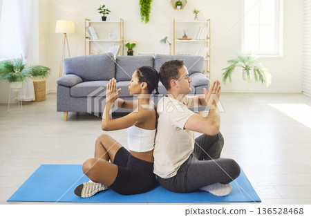 Couple meditating back to back at home on yoga mat in mindfulness together Couple meditating back to back at home on yoga mat in mindfulness together 136528468