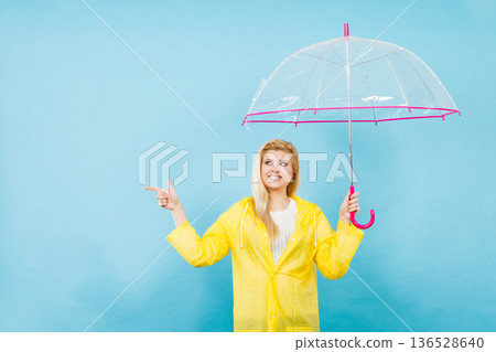 Woman wearing raincoat holding umbrella pointing Woman wearing raincoat holding umbrella pointing 136528640