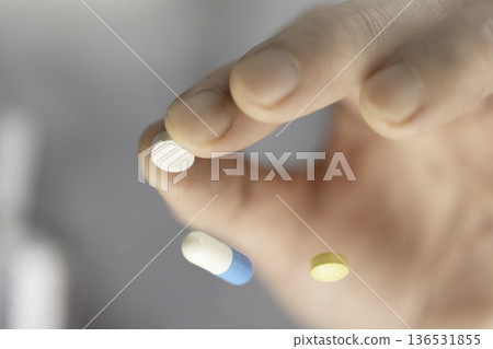 特寫鏡頭：服用前用手指捏住一顆白色藥丸。 136531855