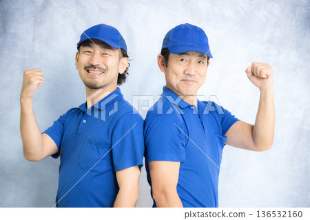 An image of two people looking at the camera and making a fist pump while moving, carrying interior goods, and luggage with their arms crossed 136532160