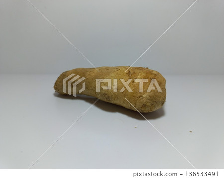 Ginger Root on White Background. Close-up of a single piece of ginger root placed on a plain white surface with a clean white background. The ginger features a rough, tan-colored exterior with natural 136533491