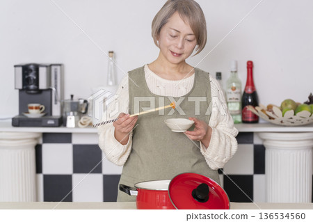 一位老婦人在廚房品嚐自己做的餐點。 一位老婦人在廚房品嚐自己做的餐點。 136534560