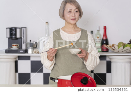 Senior woman tasting the food she cooked in the kitchen Senior woman tasting the food she cooked in the kitchen 136534561