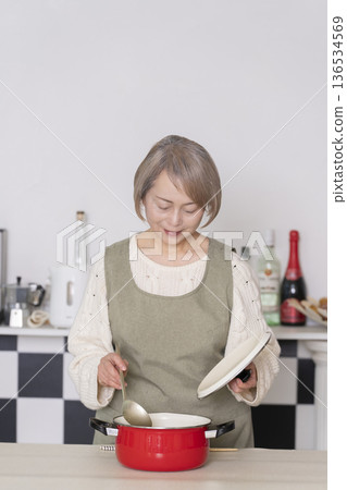 Senior woman tasting the food she cooked in the kitchen Senior woman tasting the food she cooked in the kitchen 136534569